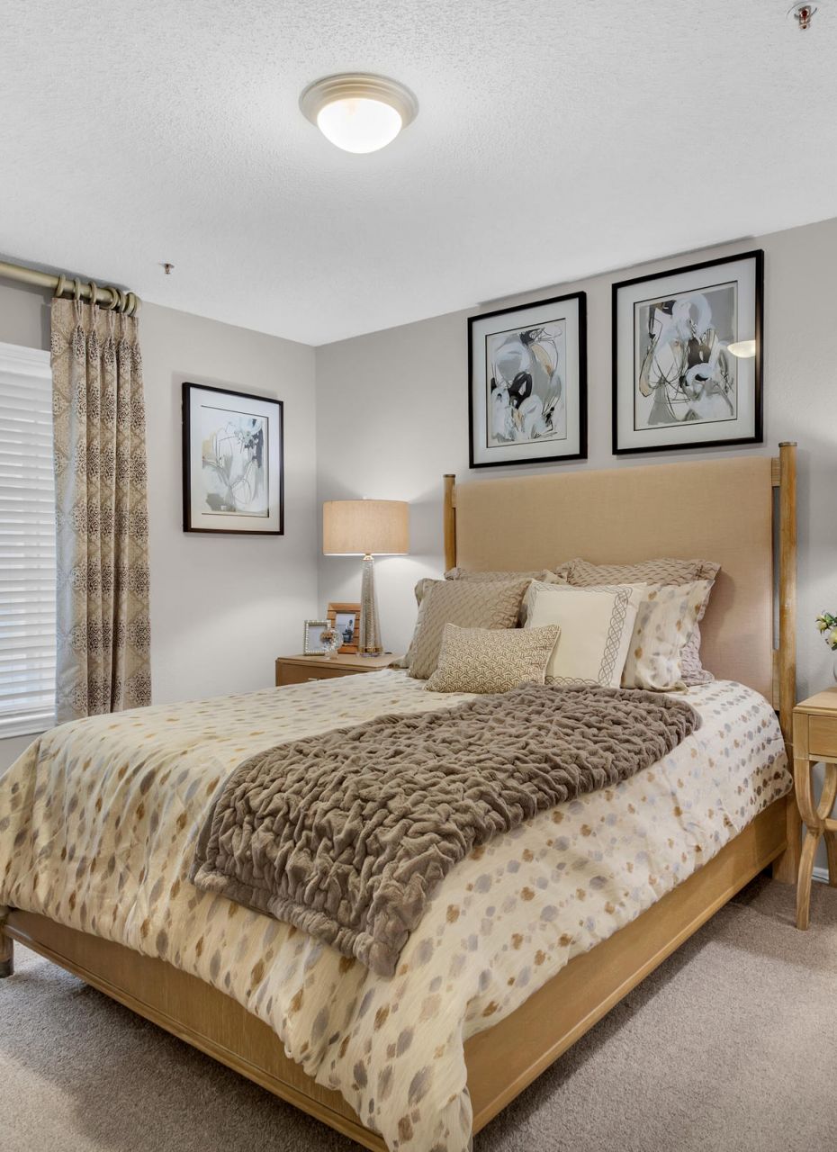 Cozy bedroom with neutral tones, a double bed, two nightstands, lamps, and framed art above the bed.