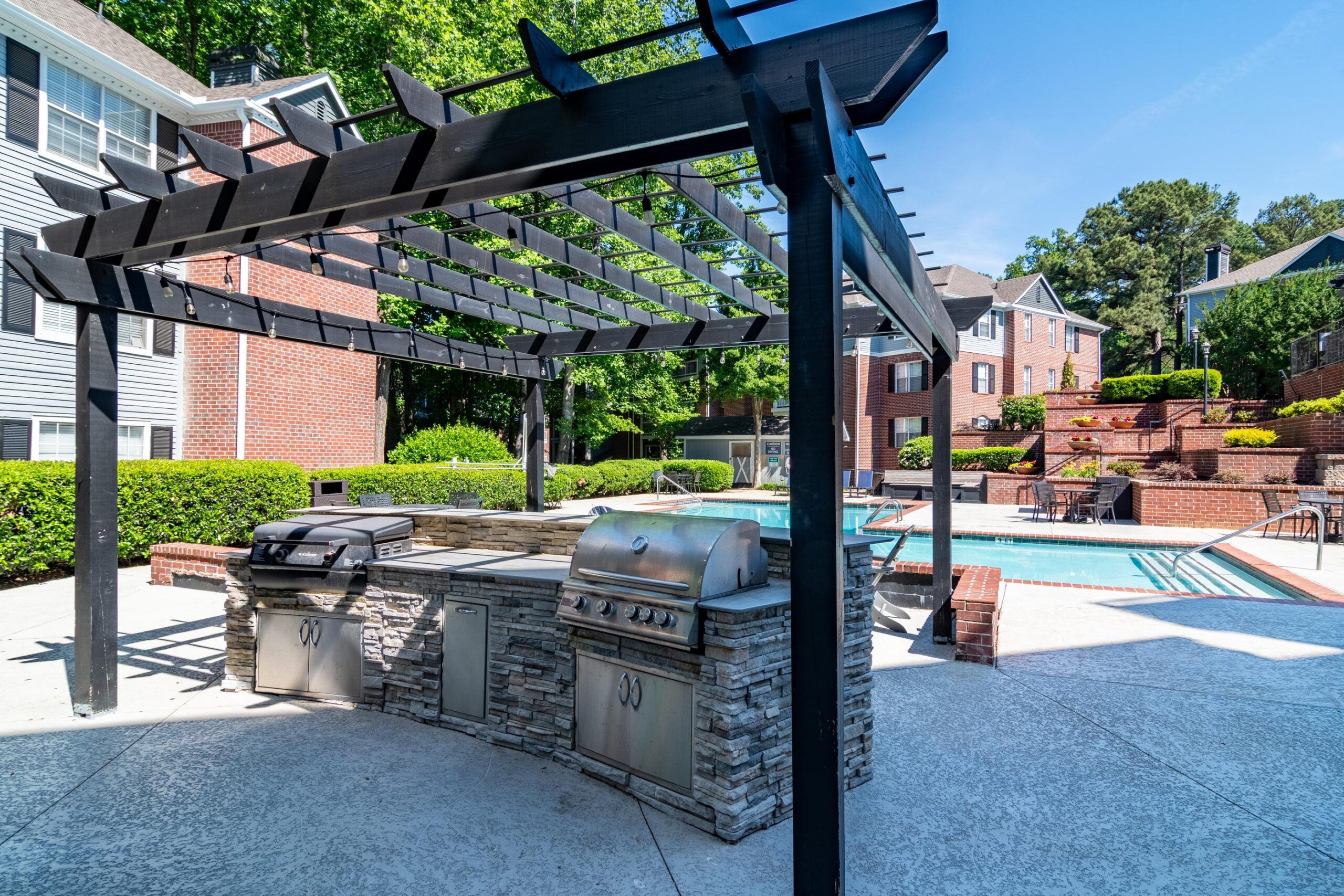 Outdoor kitchen with grills and pergola next to a swimming pool in an apartment complex courtyard.