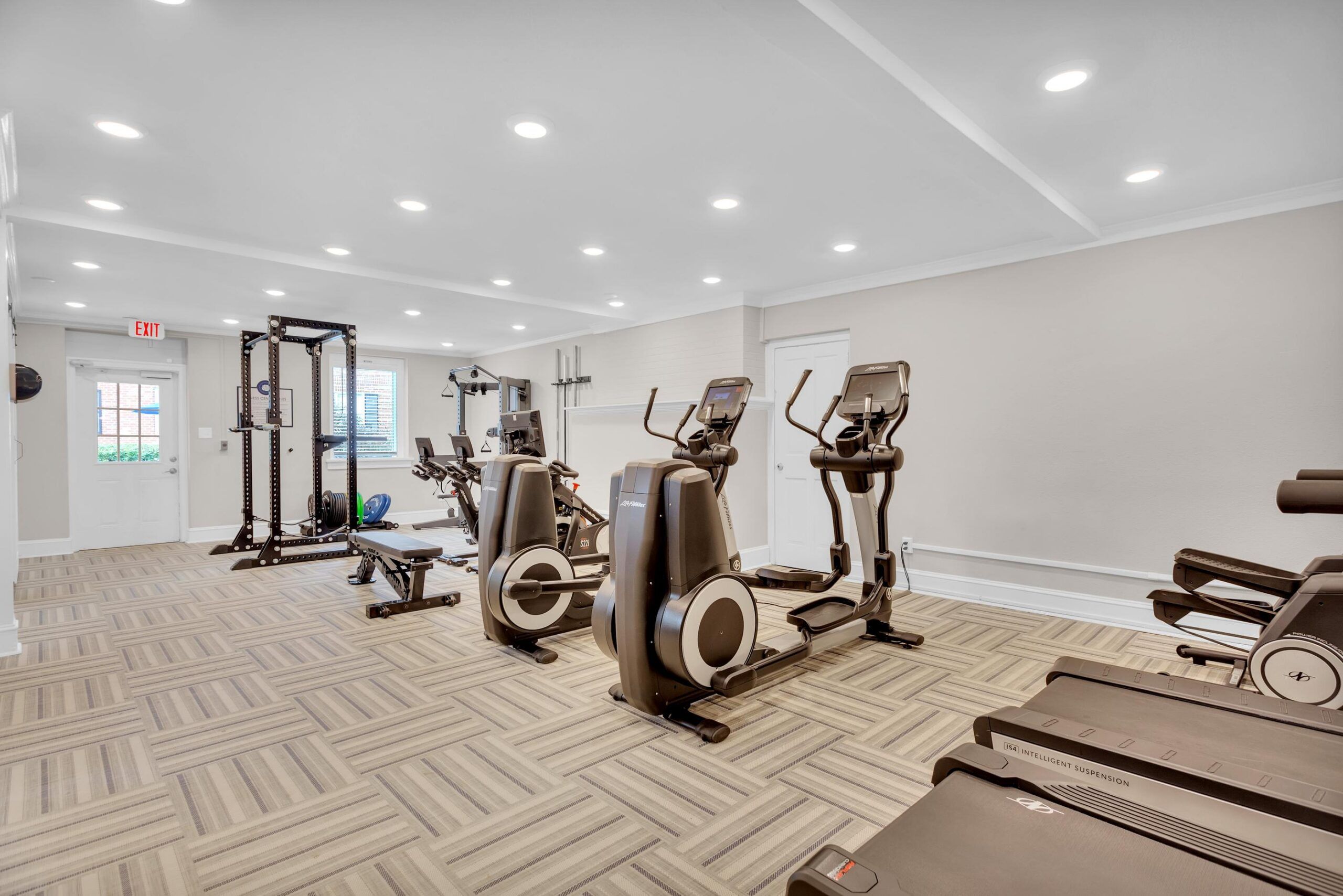 Modern gym with cardio machines, weight equipment, and bright lighting on patterned flooring.