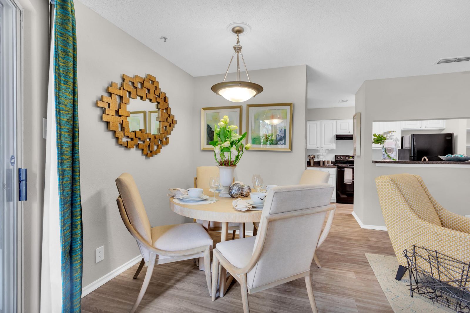 Modern dining area with round table, four chairs, wall art, and a mirror near an open kitchen.