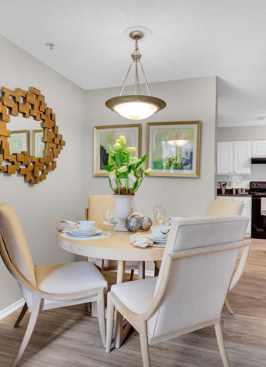 Modern dining area with round table, four chairs, wall art, and a mirror near an open kitchen.
