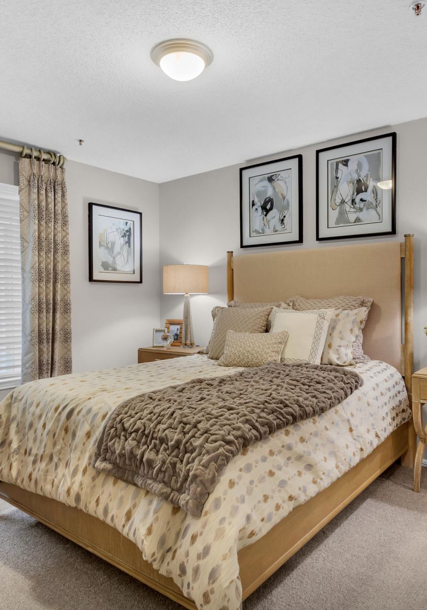 Cozy bedroom with neutral tones, a double bed, two nightstands, lamps, and framed art above the bed.