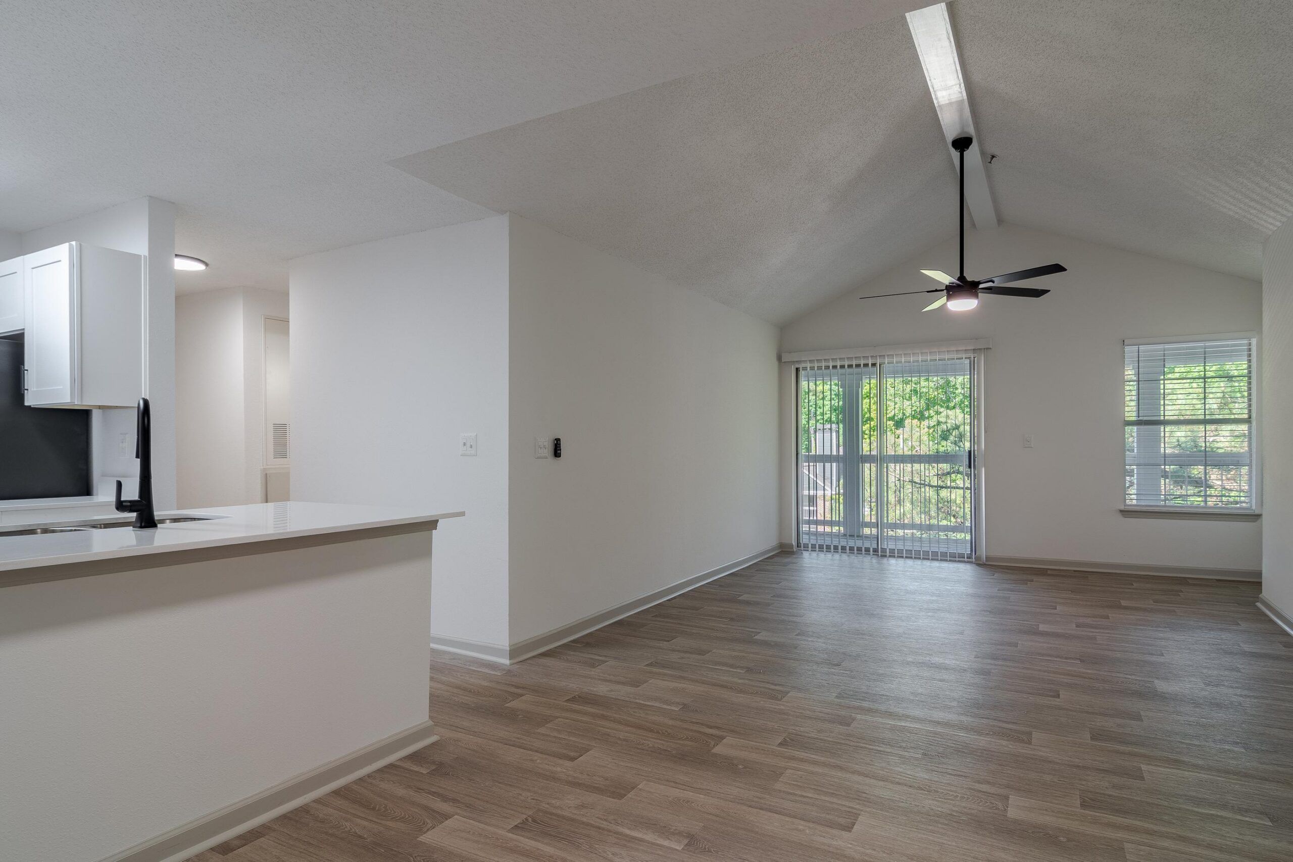 Open-plan living space with wood flooring, ceiling fan, and large windows letting in natural light.