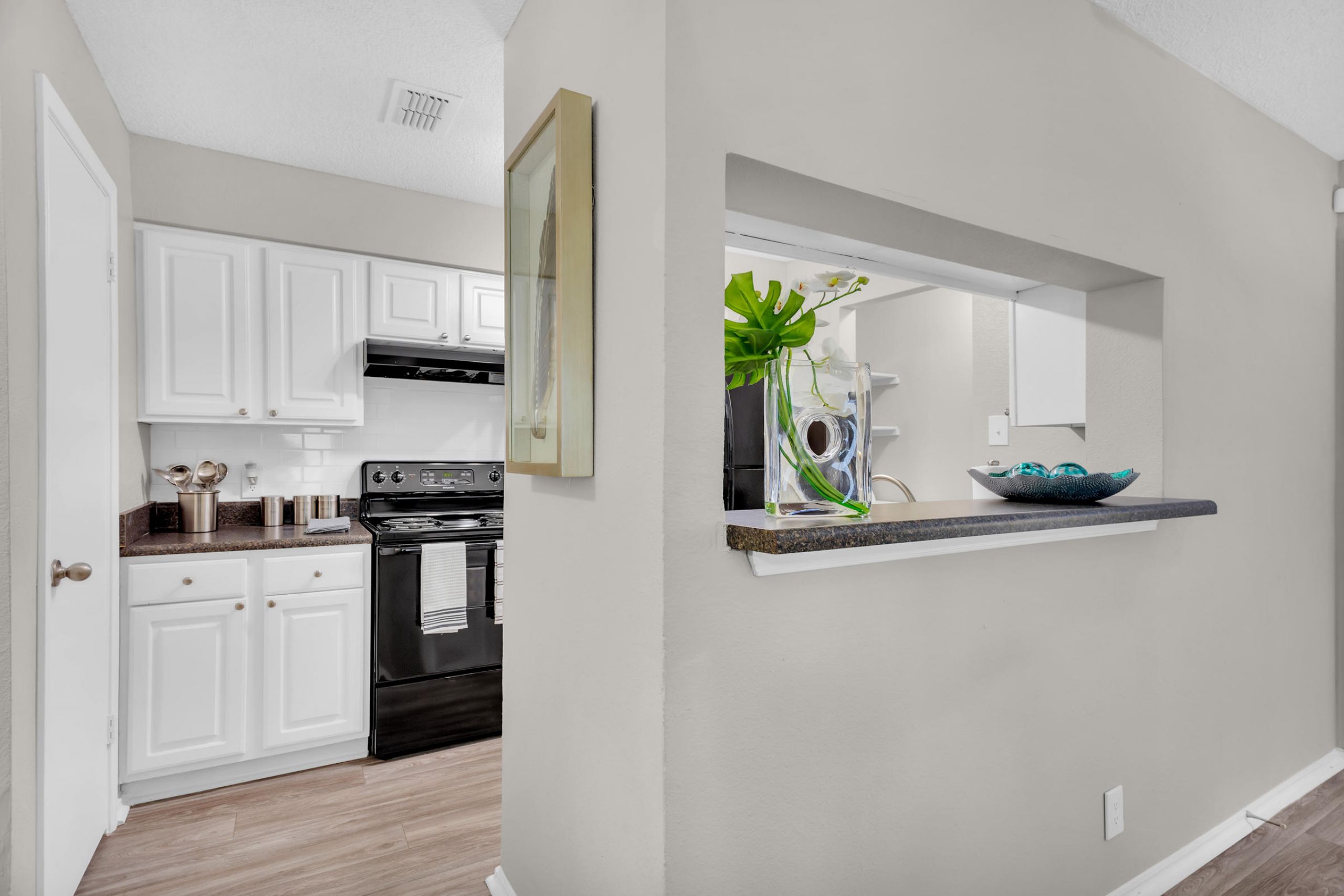 Modern kitchen with white cabinets, black appliances, and a pass-through window with decorative items on the counter.