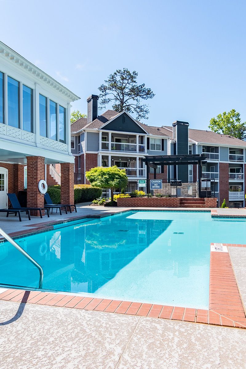 Outdoor swimming pool with clear blue water, lounge chairs, and apartment buildings in the background.