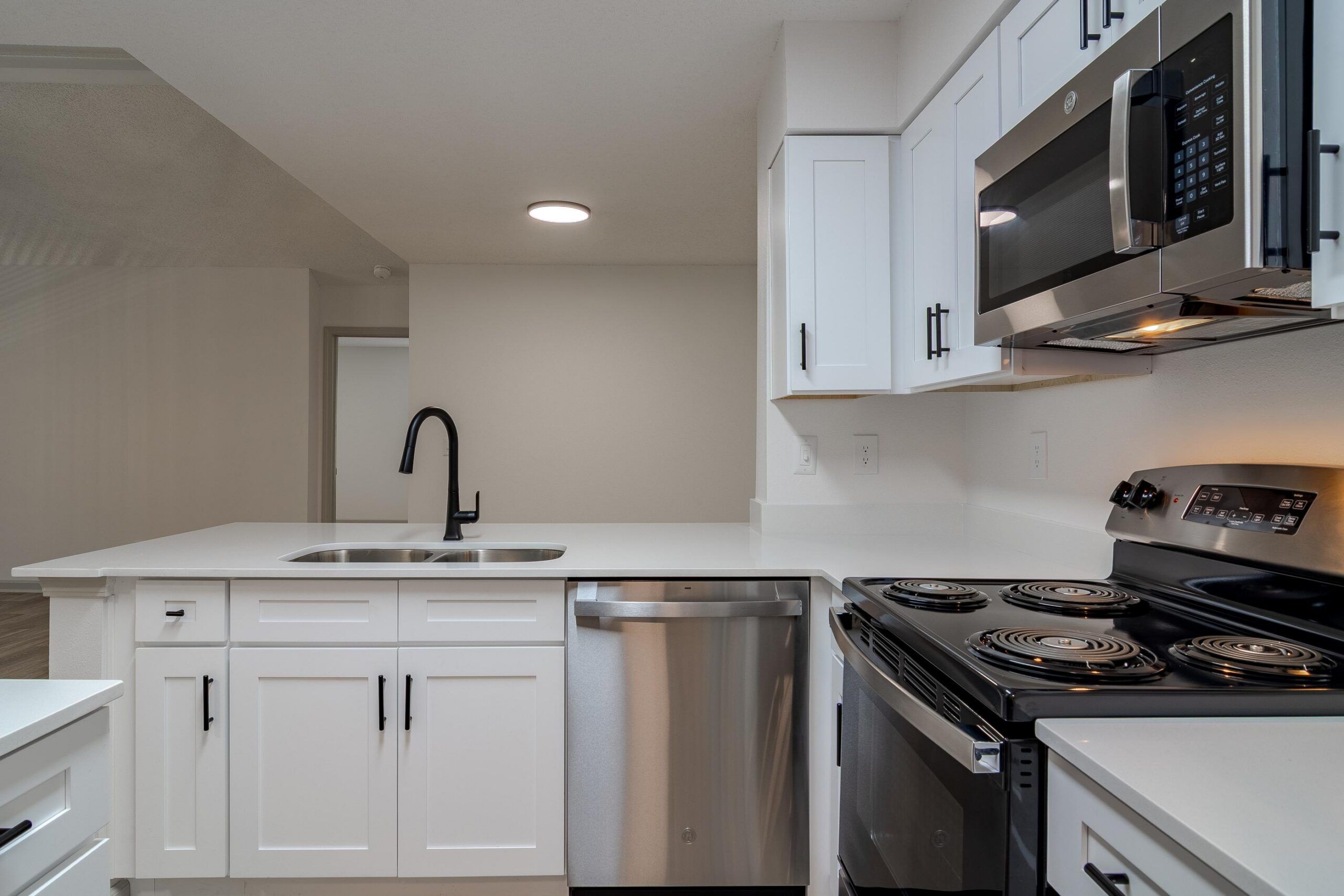 Modern kitchen with white cabinets, stainless steel appliances, and a black faucet on a white countertop.