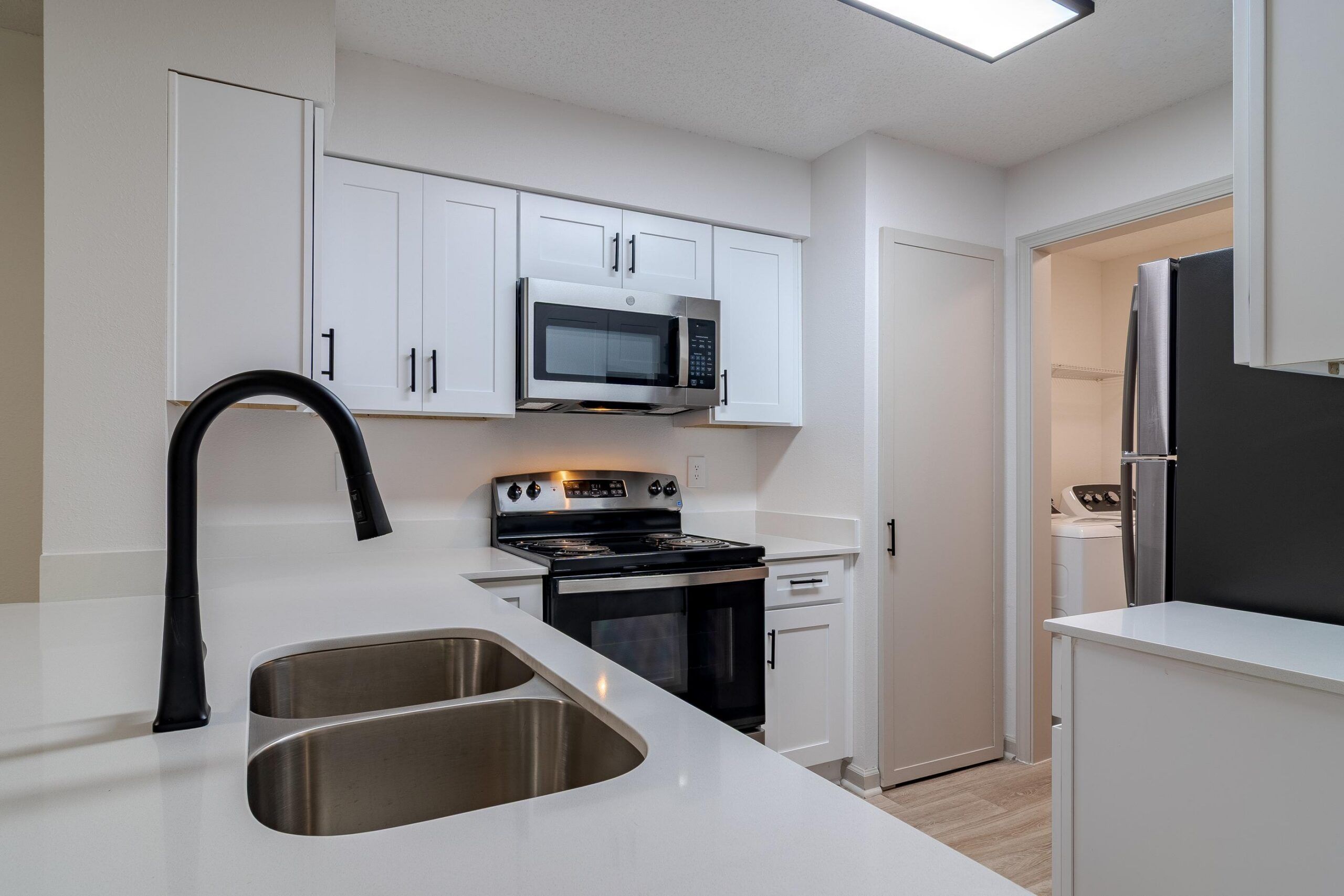 Modern kitchen with white cabinets, stainless steel appliances, and a double sink with a black faucet.