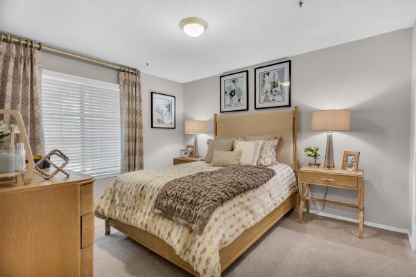 Cozy bedroom with neutral tones, a double bed, two nightstands, lamps, and framed art above the bed.