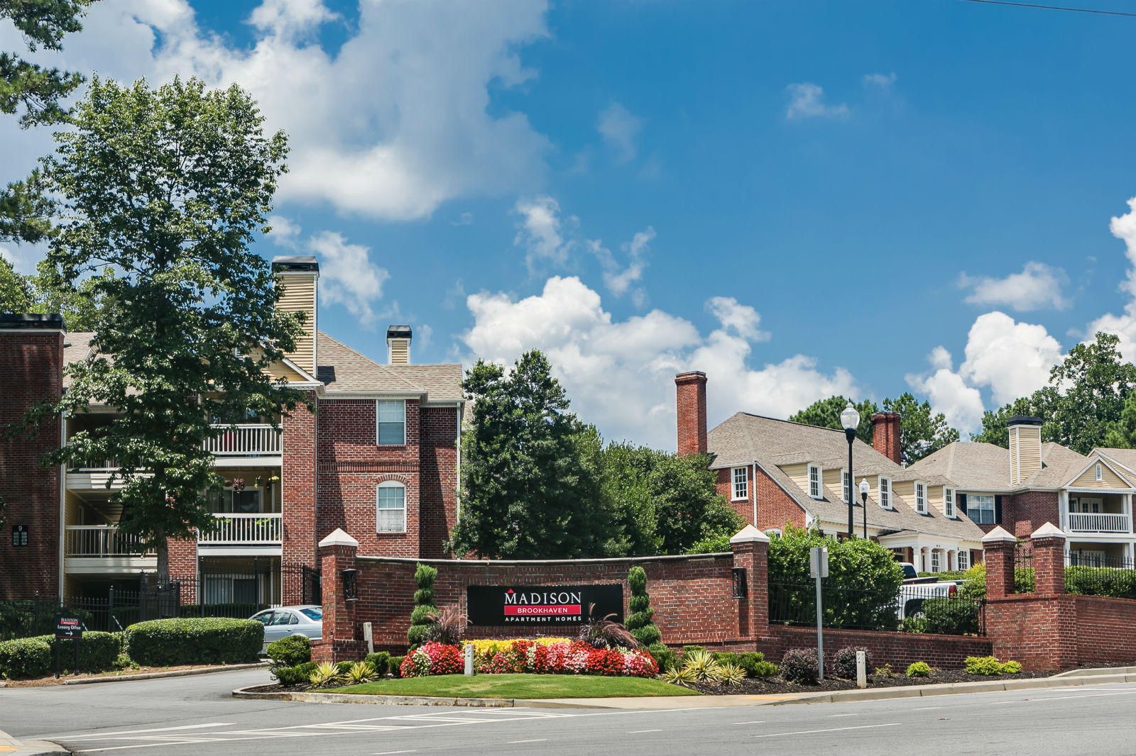 Brick apartment buildings with balconies behind a sign reading "Madison Apartments" and landscaped greenery.