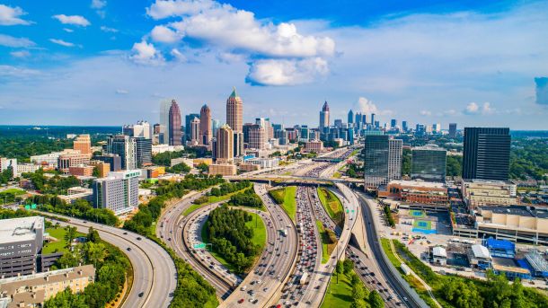 Aerial view of downtown Atlanta with highways, tall buildings, and a partly cloudy sky.