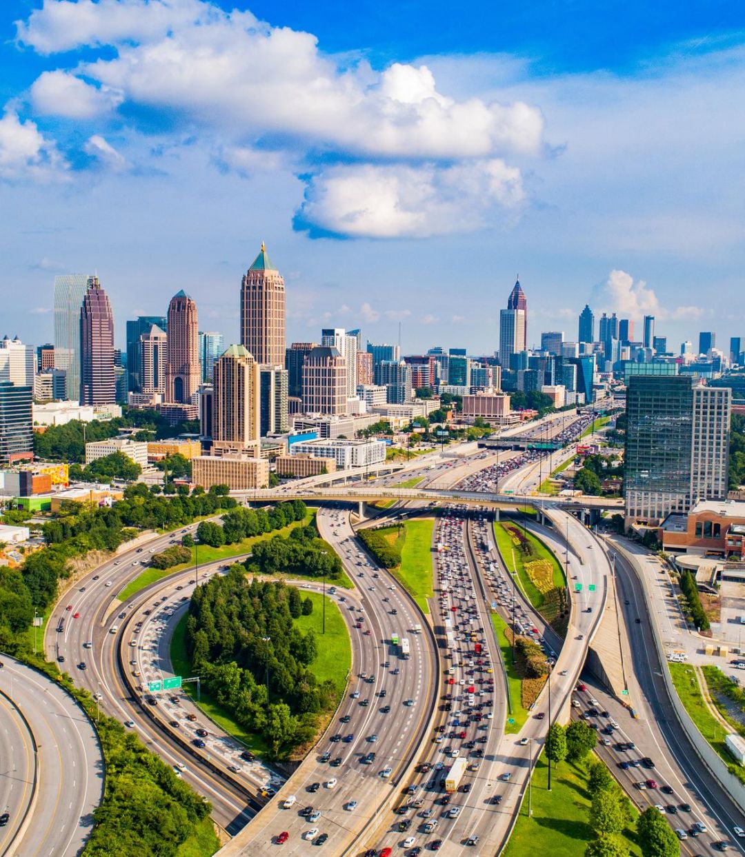 Aerial view of downtown Atlanta with highways, tall buildings, and a partly cloudy sky.