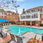 Outdoor pool area with lounge chairs and umbrellas, next to a large brick building and clear blue sky.