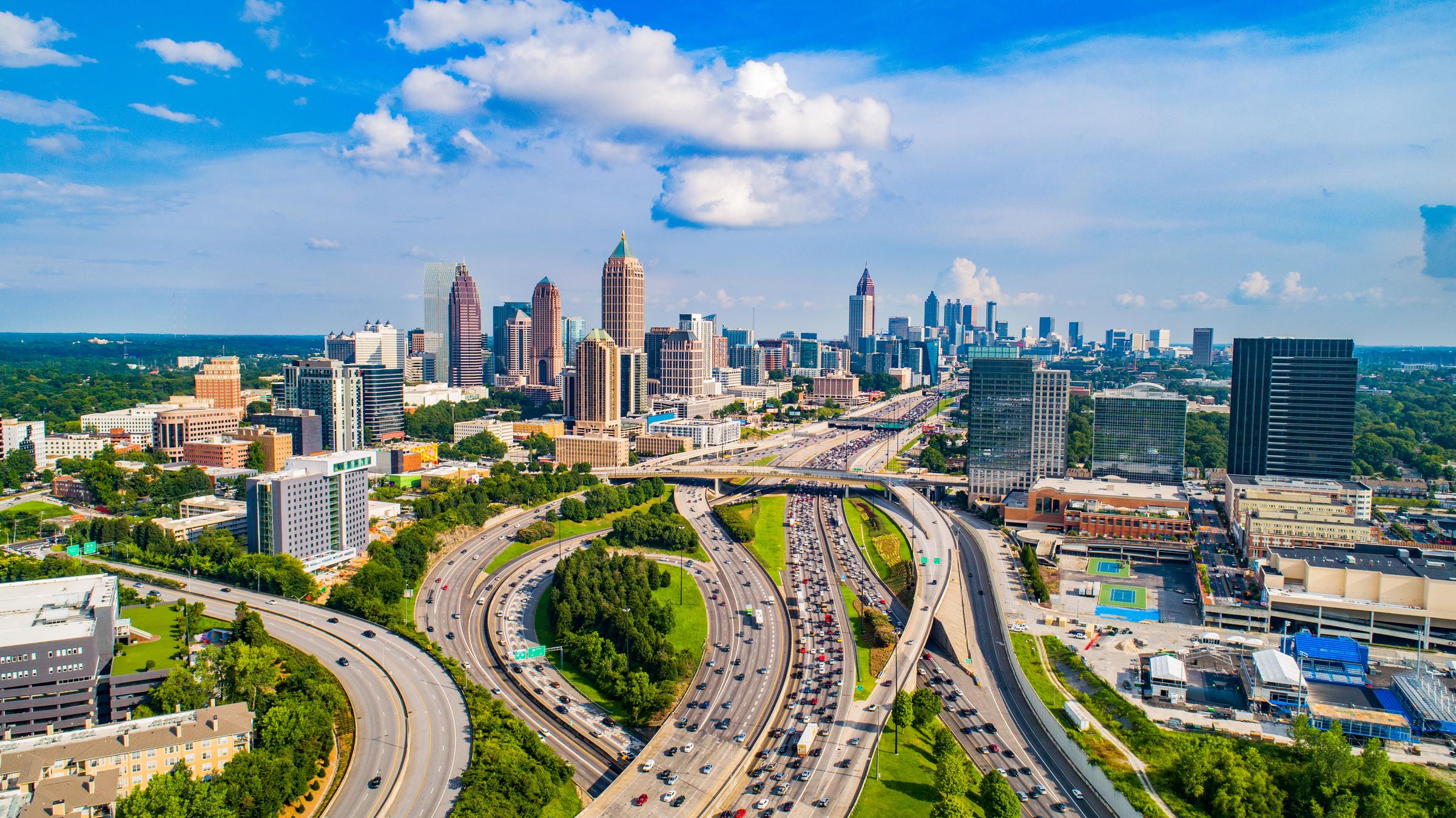 Aerial view of downtown Atlanta with highways, tall buildings, and a partly cloudy sky.